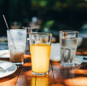 a glass of water, orange juice and coffee served on table in an outdoor restaurant against beautiful sunlight