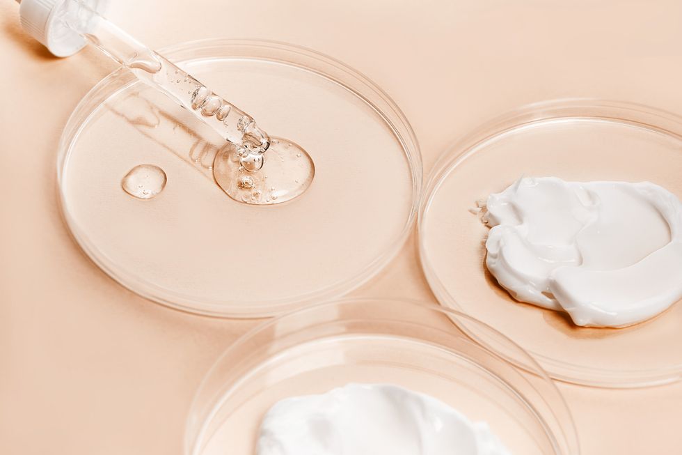 glass pipette with face serum or essential oil with oxygen aqua bubbles and a drop of liquid and white colour smear of face cream, hand cream in petri dishes on a pastel beige orange background with shadow in peach color