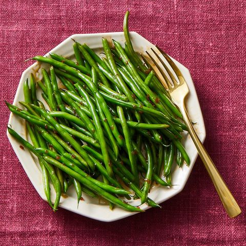 glazed green beans with a gold fork on a white plate