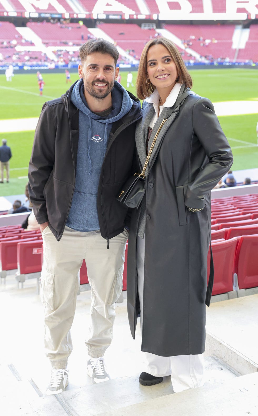 la pareja, vestida de invierno, en las gradas de un campo de futbol