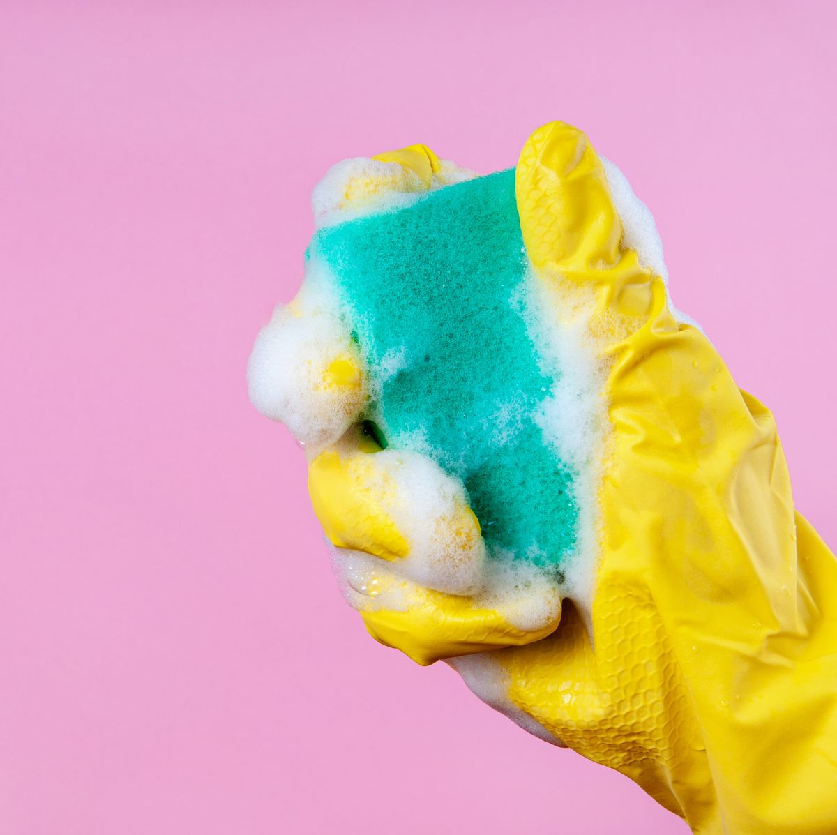 gloved hand holds a foam sponge on a pink background copy space