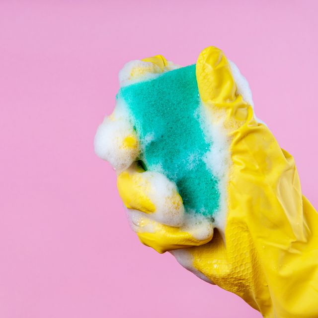 gloved hand holds a foam sponge on a pink background copy space