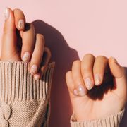 glowing hands in sweater with knitted sleeves and with nude color manicure with gold particles on pink table