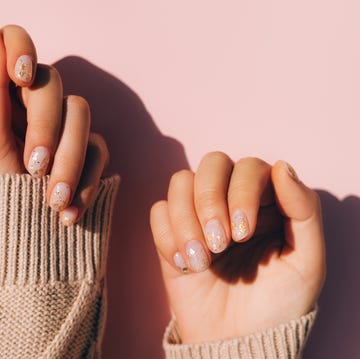 glowing hands in sweater with knitted sleeves and with nude color manicure with gold particles on pink table trendy colors of the year