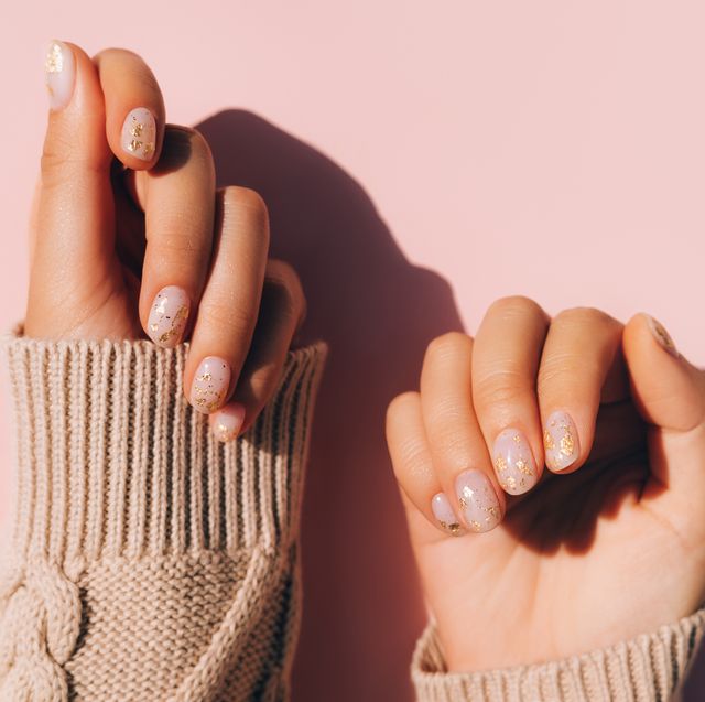 glowing hands in sweater with knitted sleeves and with nude color manicure with gold particles on pink table trendy colors of the year
