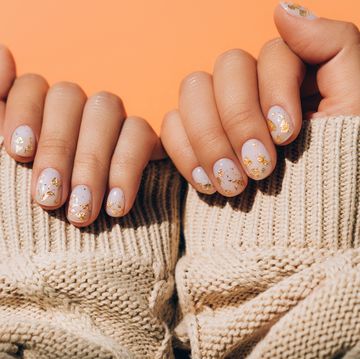 glowing hands in sweater with knitted sleeves and with nude color manicure with gold particles on orange table trendy colors of the year