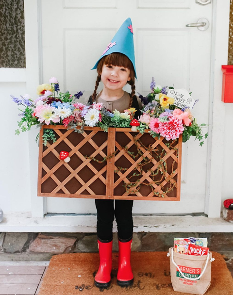 young girl in braids wearing paper gnome hat, rainboots, and diy box costume covered in trellis and filled with faux flowers