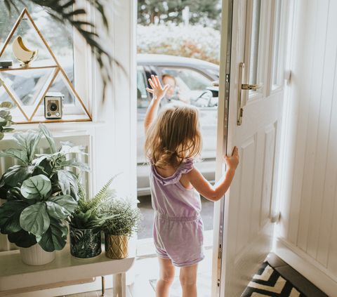 cute little girl waving out the door in a sunny hallway