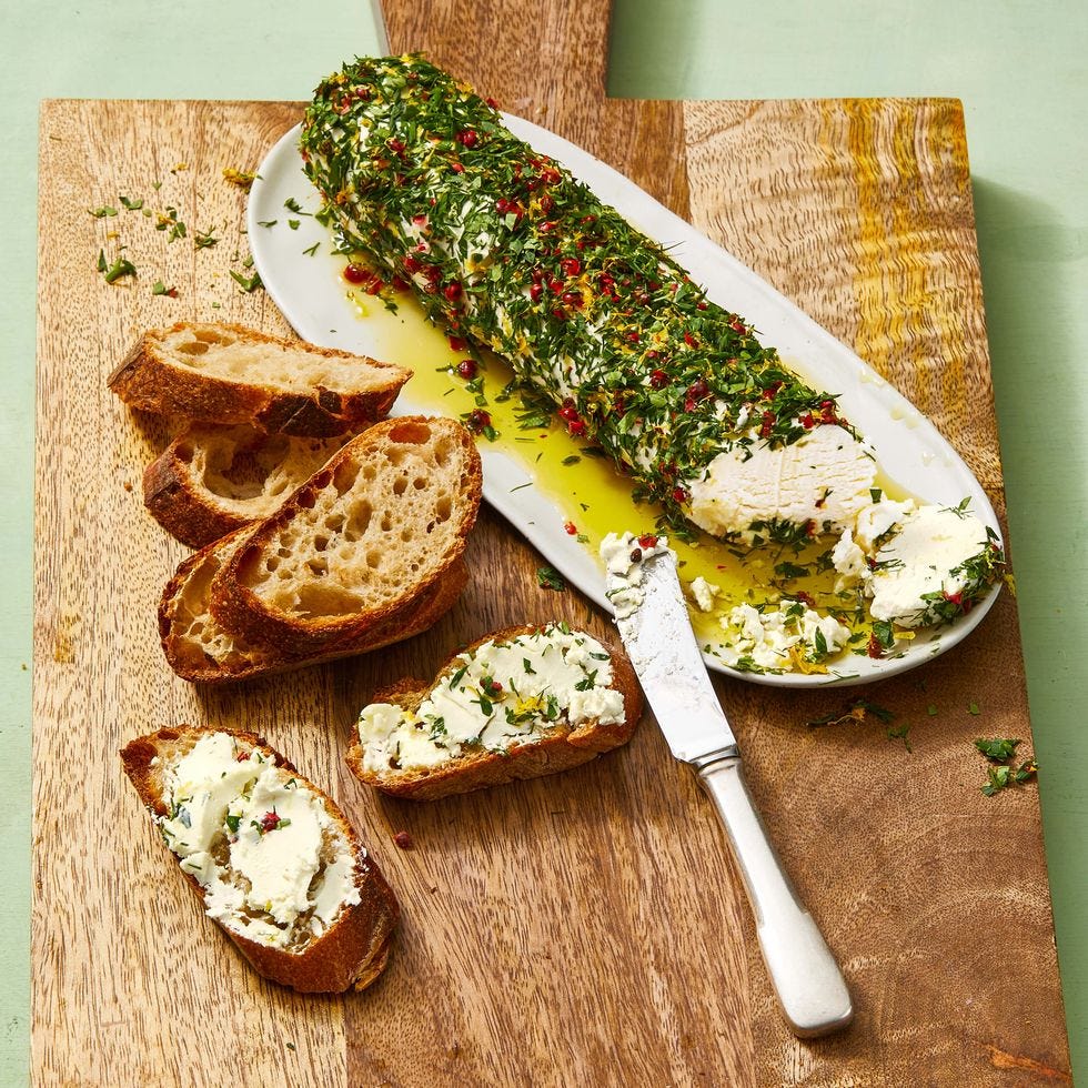 a green herby log of goat cheese on a white plate with slices of crusty toast
