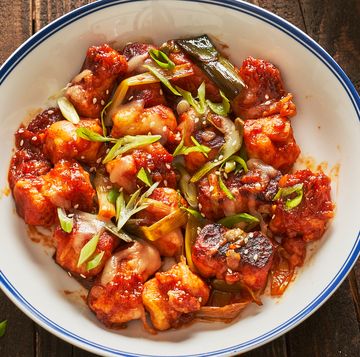a white bowl of gnocchi in gochujang red sauce topped with scallions and sesame seeds on a wood background