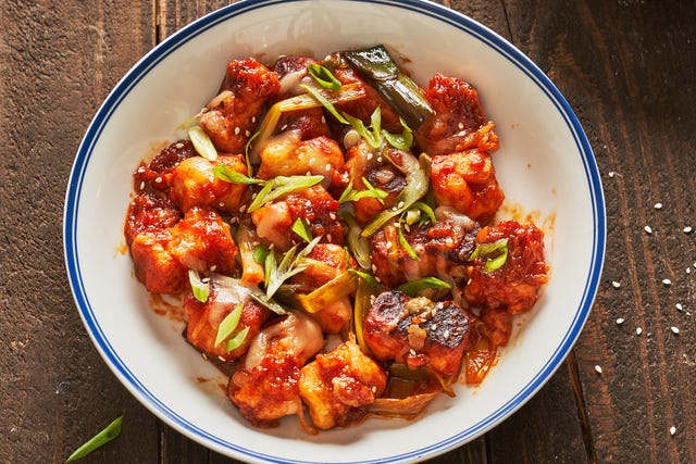 a white bowl of gnocchi in gochujang red sauce topped with scallions and sesame seeds on a wood background