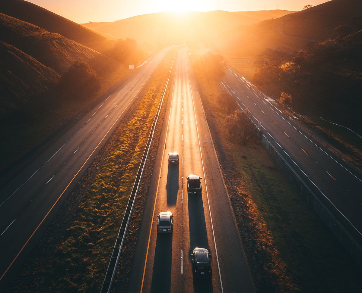 golden light illuminates a remote highway with four cars on it
