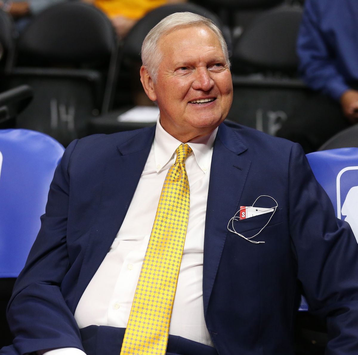 jerry west sitting courtside at a basketball game with the nba logo on chairs