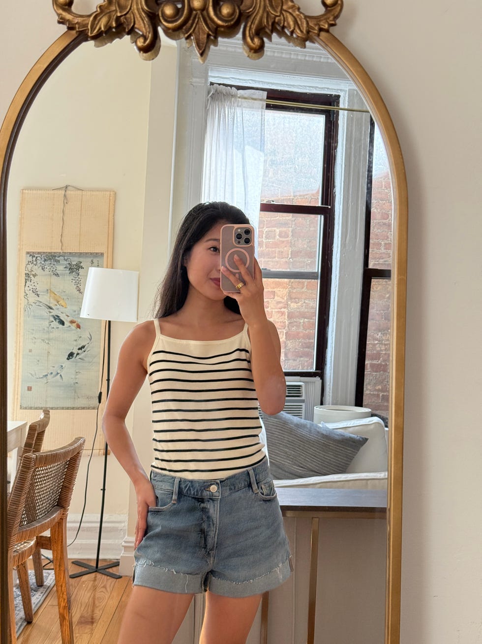 person in a striped tank top and denim shorts posing in front of a mirror