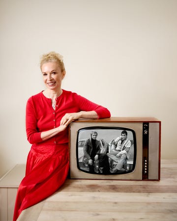 an individual in a red outfit sitting beside a vintage television displaying a black and white scene