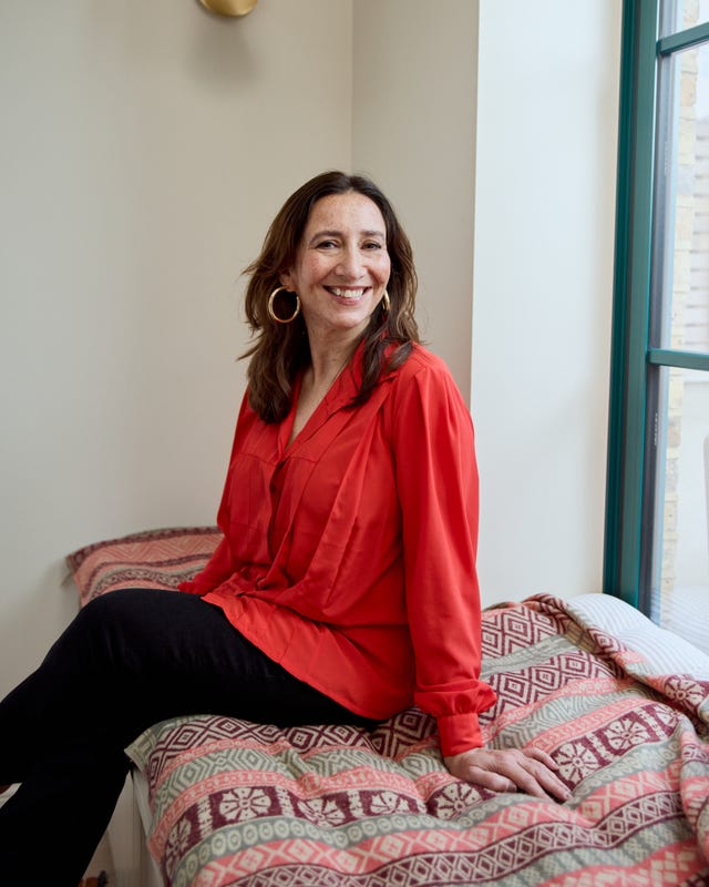 a woman in a red blouse seated on a patterned bed