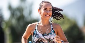 good looking woman brunette runs with a water bottle in hand and headphones on