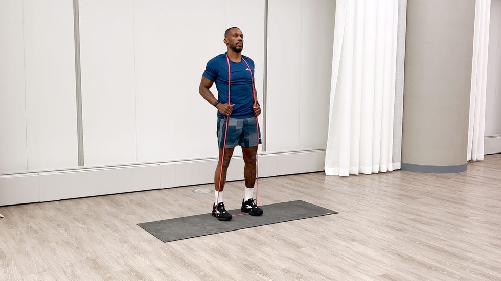 man performing good morning exercise with a resistance band while standing on an exercise mat in a gymlike enviroment.