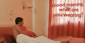 a man lounging in bed looks at a curtain with the words "good morning what are you wearing" projected on it