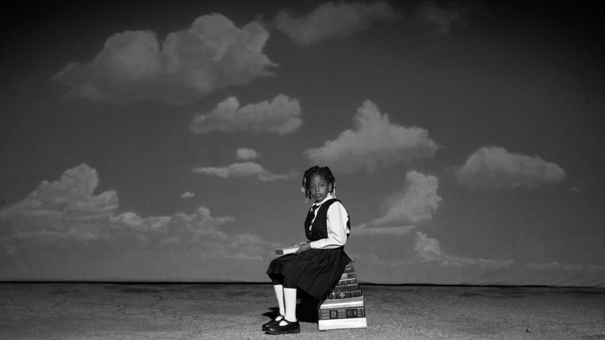 a child seated on a stack of books against a backdrop of clouds
