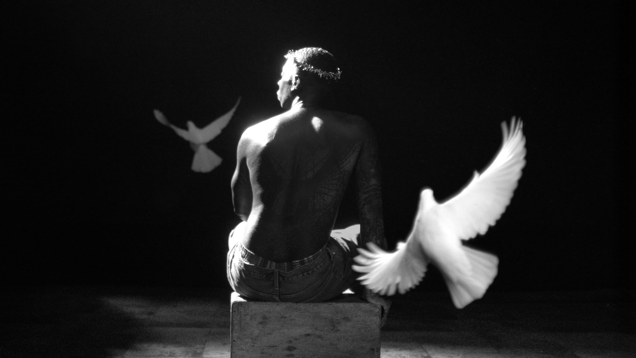 individual seated on a block with doves in flight around them