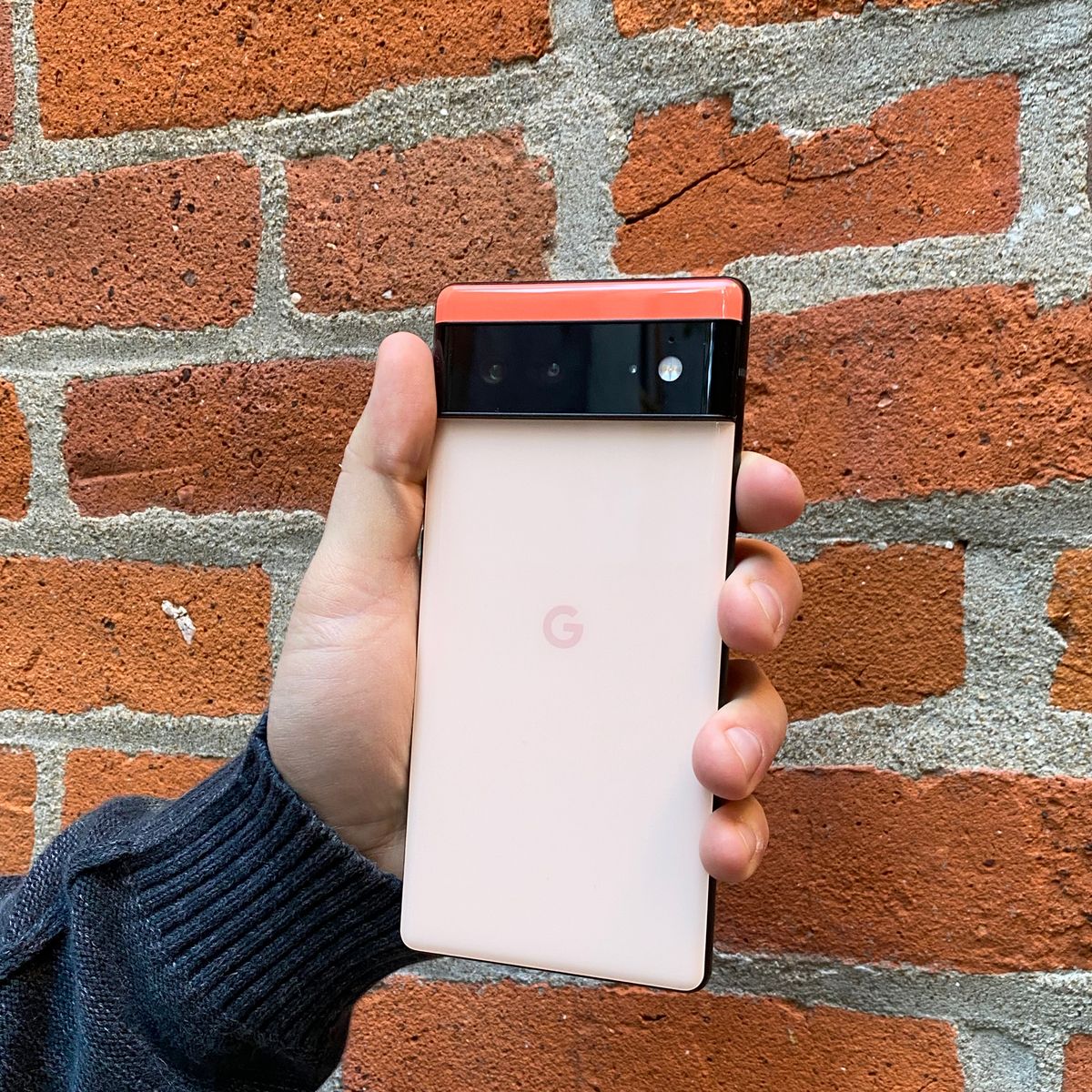 hand holding coral google pixel 6 in front of brick wall