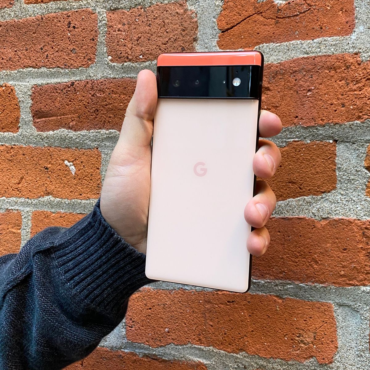 hand holding coral google pixel 6 in front of brick wall