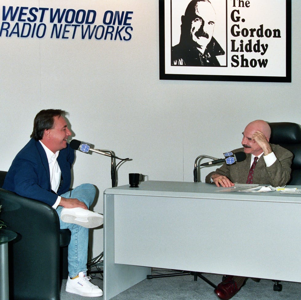g gordon liddy sitting at a radio microphone interviewing a guest