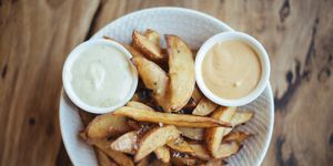 Gourmet potato wedges served with black sea salt & aioli in a white bowl, shot directly above