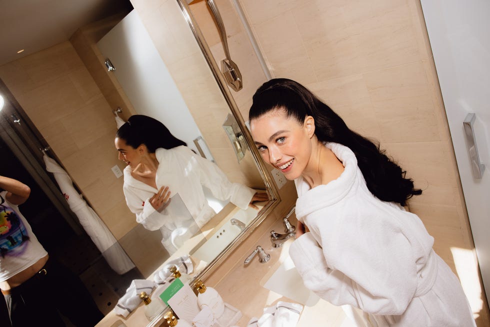 a bathroom setting with a person in a white bathrobe and a reflection in the mirror