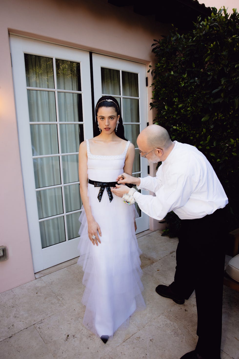 a woman in a formal white dress is being assisted with her outfit by a man in a collared shirt