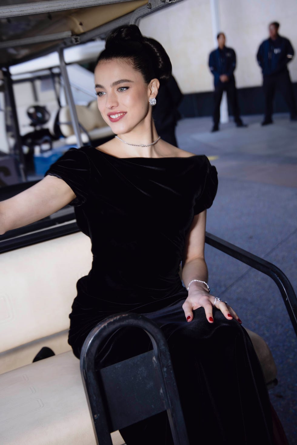 woman in elegant dress seated on a vehicle with security personnel in the background