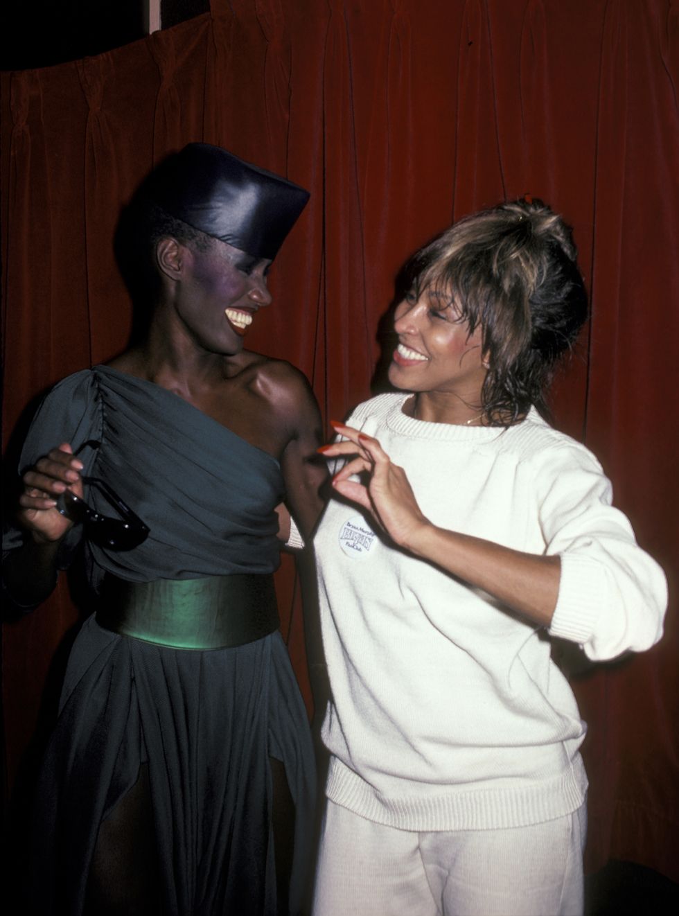 grace jones and tina turner smile as they look at each other