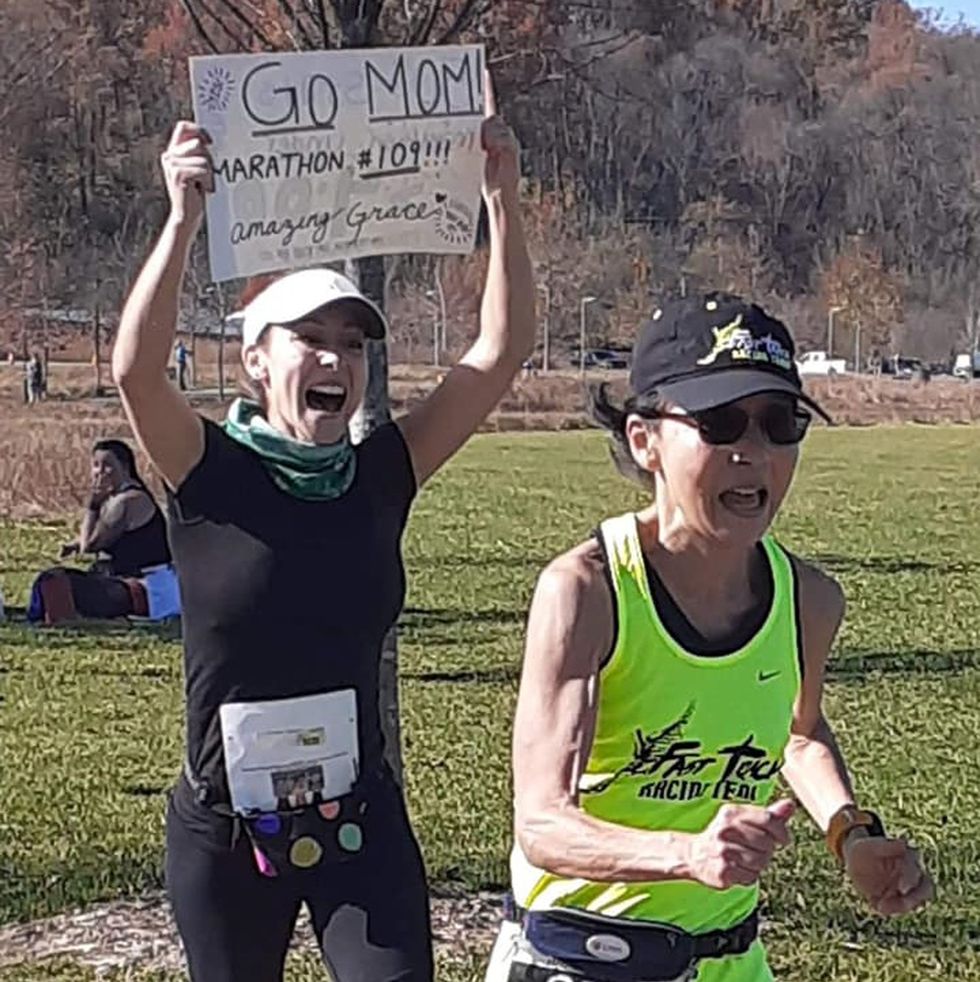 a woman running a race followed by another runner carrying a sign reading go mom marathon 109