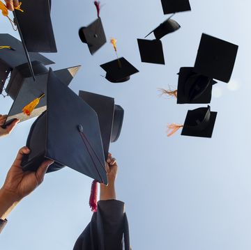 cropped hands of people throwing mortarboards against clear sky