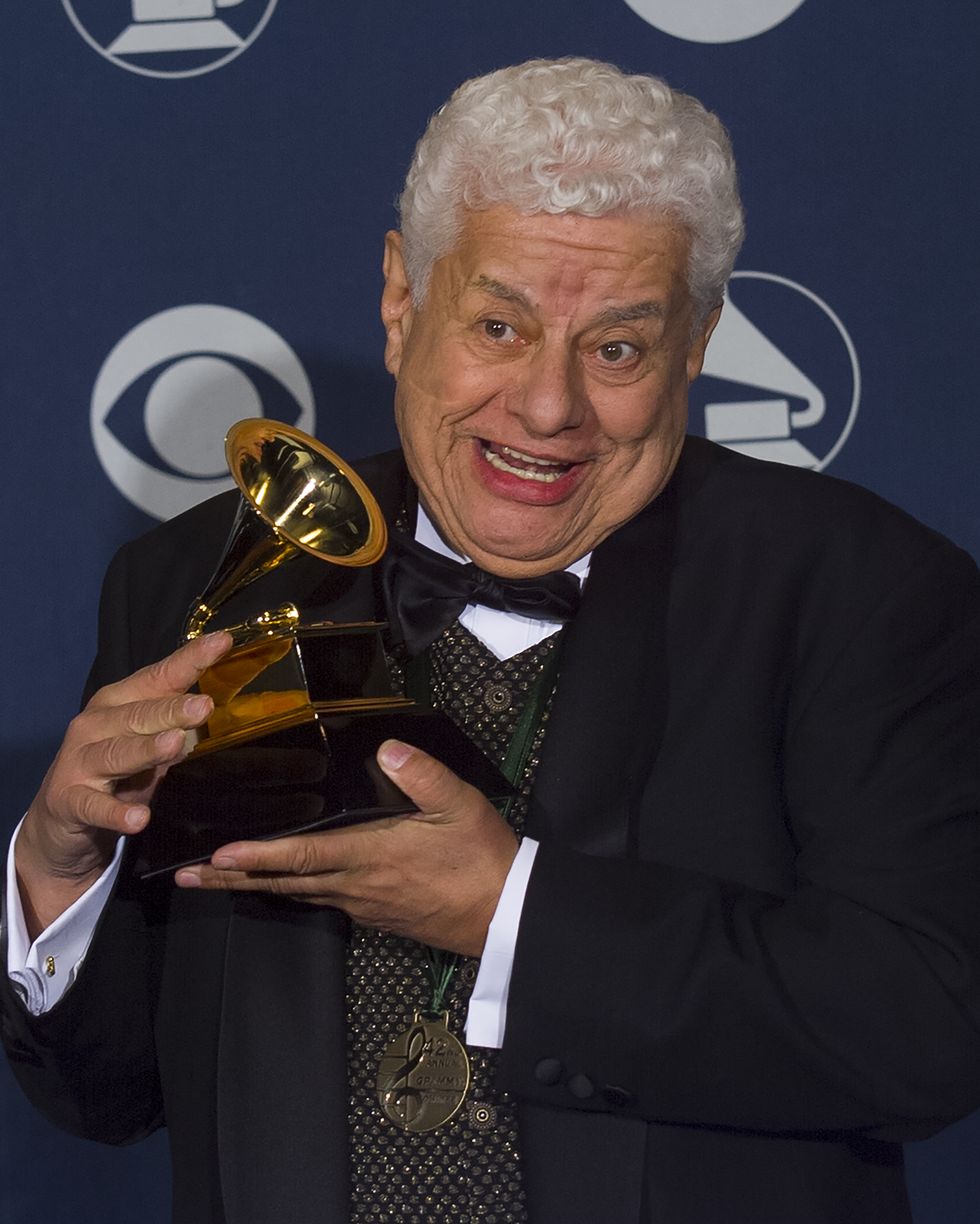 a man in a black three piece suit smiles while holding up a grammy award