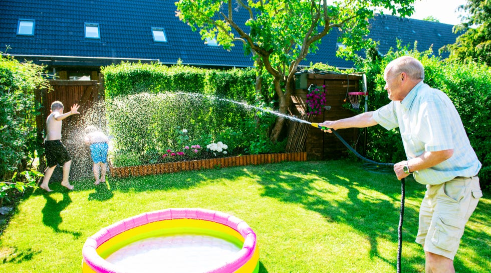 grandfather sprays water on grandchildren with garden hose for fun