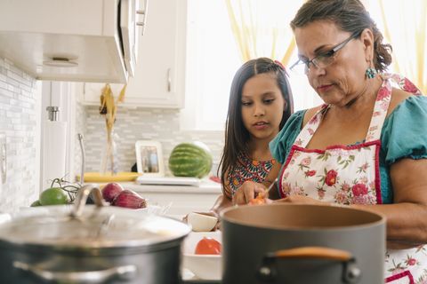 grandmother teaching granddaughter to cook in kitchen at home