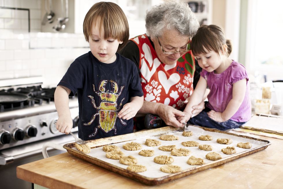 grandma and two young grandchildren baking the granddaughter is placing dough on a cookie sheet with grandmothers help