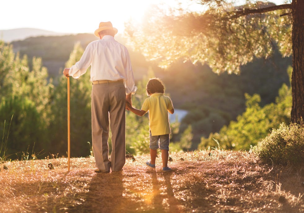 back view or grandfather with cane holding hand of his young grandson while on a walk