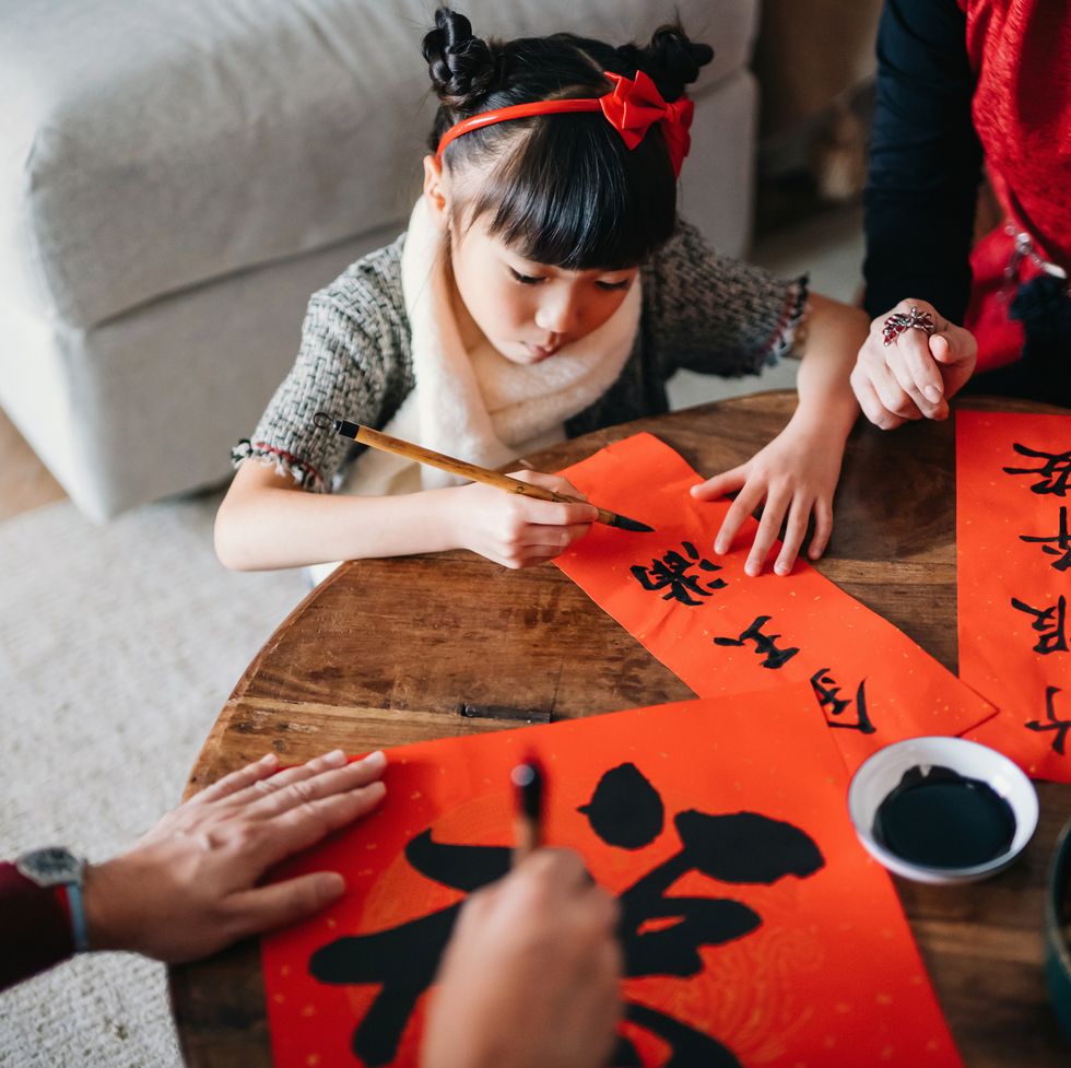 grandparents practising chinese calligraphy for chinese new year fai chun auspicious messages and teaching their granddaughter by writing it on couplets at home