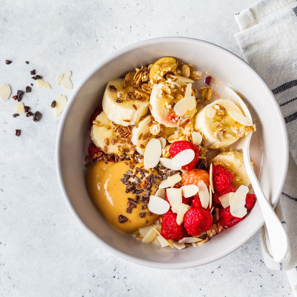 granola with berries, banana, peanut butter and chocolate in a white bowl