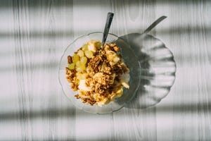 granola with yogurt and fruits in a glass plate, top view