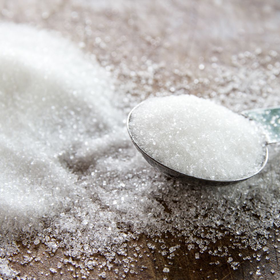 granulated sugar in spoon and sugar pile on wooden
