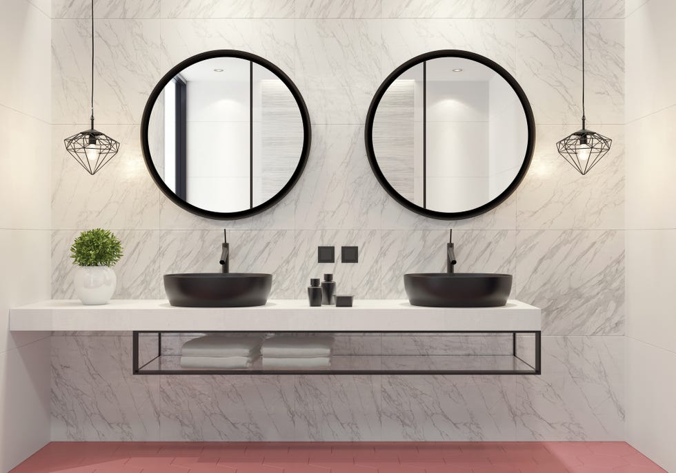 luxurious bathroom with light pink honeycomb ceramic tiles and light gray and white large matte ceramic tiles. long vanity unit with white corian stone finish, metal black shelf and round black ceramic washbasin, stainless steel waterfall vanity sink faucet and a decorating plant. walk in shower with light large ceramic tiles, stainless steel black shower panel, decorating wall shelf and natural stone dark gray narrow long floor tiles.
