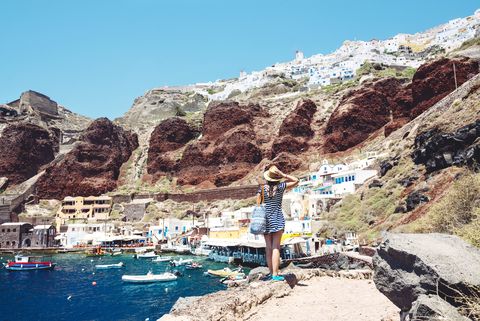 greece, santorini, oia, woman enjoying the view in the fishing harbor with the white village above the cliff