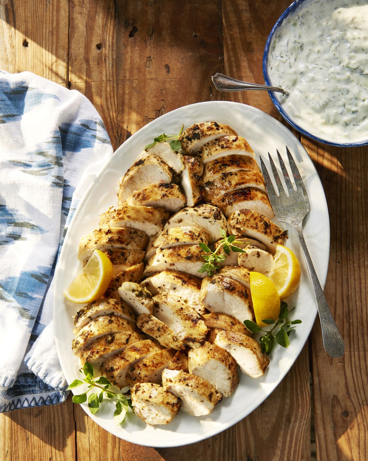 greek chicken sliced on a plate with lemon wedges and tzatziki sauce
