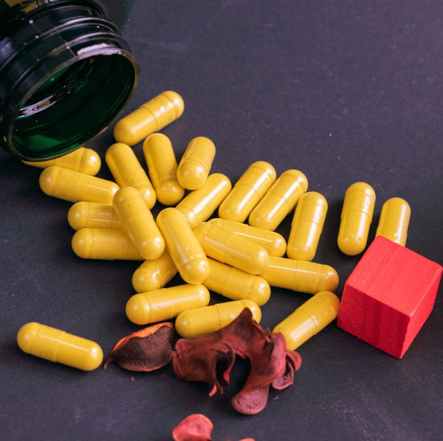 green bottle of supplements with yellow capsules on a black background