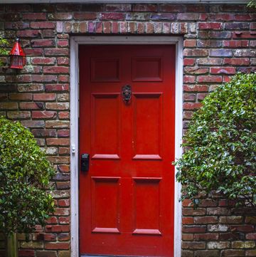color photograph of a red front door, brick house and green bushes surrounding