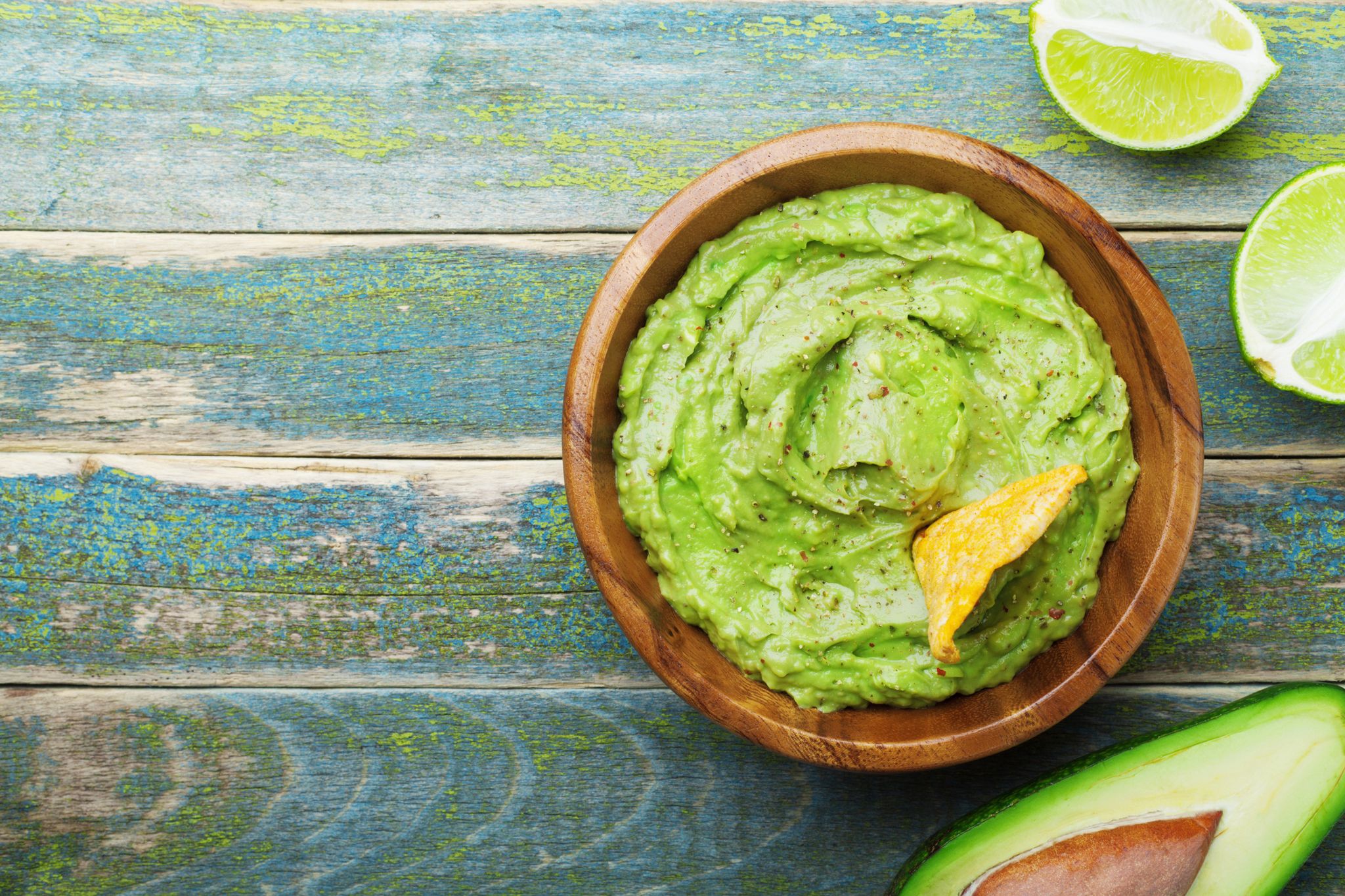 green guacamole with  ingredients avocado, lime and nachos on wooden vintage table top view